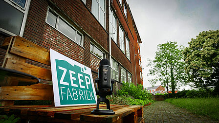 Foto van een bord met het logo van de Zeepfabriek, met daarbij een podcast microfoon. De foto is genomen voor de Zeepfabriek.